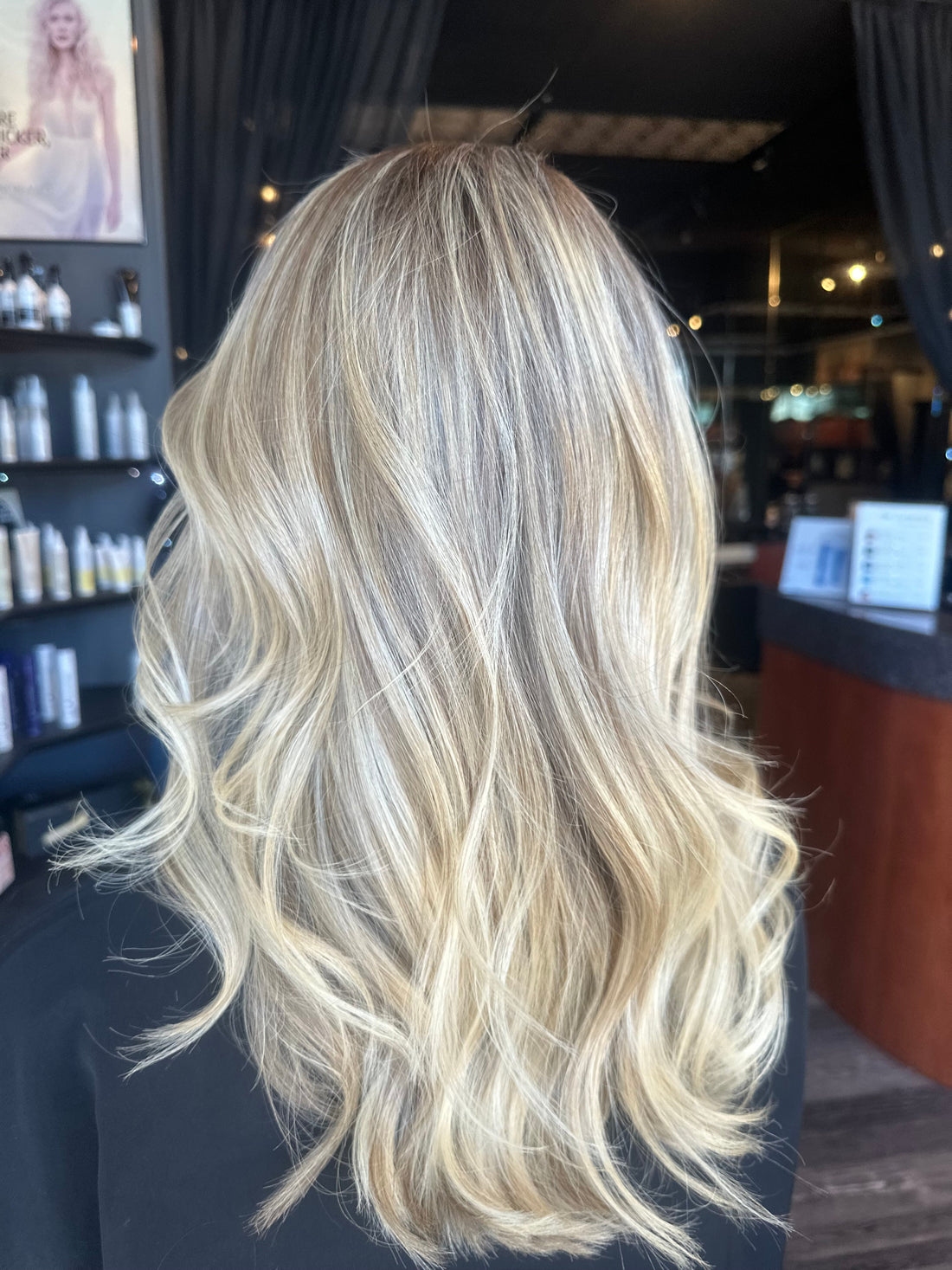 Long, softly layered blonde hair styled in loose waves with a bright, creamy finish